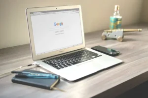Laptop Google-lal, telefon, jegyzetfüzetek és dísztárgyak íróasztalon.