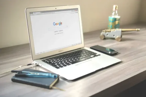 Laptop Google-lal, telefon, jegyzetfüzetek és dísztárgyak íróasztalon.