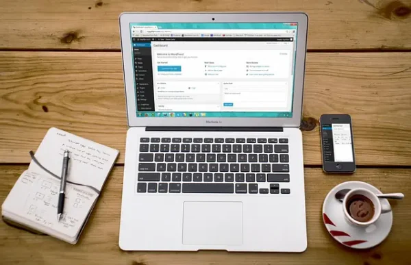 Laptop WordPress-szel, kávé, jegyzetfüzet fa asztalon